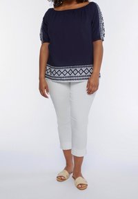 Navy blue off-the-shoulder top with puffed sleeves and geometric white pattern along the hem, paired with white cropped pants and light sandals.