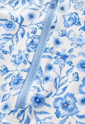 Stoff mit Blumenmuster in Weiß und Blau, mit einem hellblauen Reißverschluss. Enthält detaillierte blaue Blumen und Blätter, mit glatter Textur.