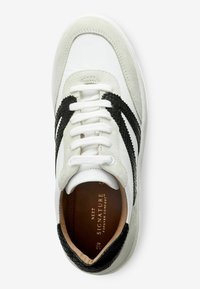 Sneaker bianca con accenti neri testurizzati, dettagli in suede e lacci piatti. Presenta una punta arrotondata e una soletta ammortizzata.