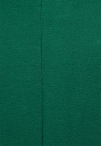 Tecido verde com uma superfície lisa e texturizada. O tecido apresenta uma costura vertical pelo centro, criando secções distintas.