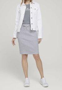 Veste en denim blanche, top rayé bleu marine et blanc, jupe en jersey grise à mi-longueur avec cordon de serrage, et baskets blanches. Ensemble simple et décontracté.