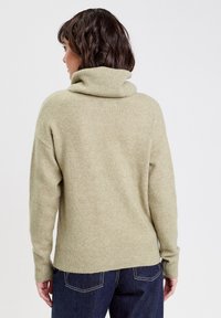 Pull léger en olive clair avec un col roulé côtelé, texture douce et coupe décontractée ; il possède des manches longues et un ourlet large.