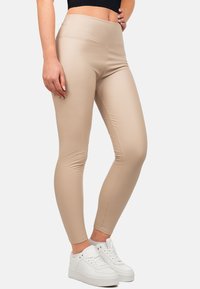 Leggings beige con vita alta, texture liscia e forma aderente, abbinati a sneakers bianche per un look casual.