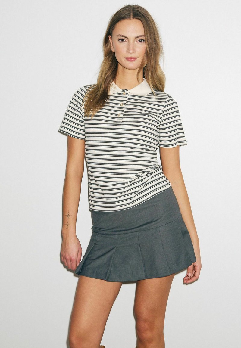 Polo rayé crème et marine avec une patte de boutonnage, associé à une mini-jupe plissée grise. Tissu lisse avec une silhouette ajustée.