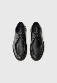 Zapatos de cuero negro con puntas redondeadas, costuras decorativas y cordones delgados. Textura suave, plantillas blandas y suelas de goma.