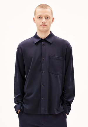 Donkerblauwe langarmsgemiddelde shirt gemaakt van zachte stof, met een knoopsluiting aan de voorkant, een kraag en een borstzak met een subtiele logo-accentuering.