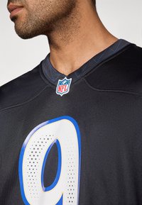 Μαύρη φανέλα NFL με μπλε και λευκό αριθμό «9», με λογότυπο στο λαιμό και λεπτομερή ραφή κατά μήκος του γιακά.