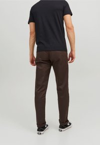 Ruskeat puuvillahousut, joissa on kapeahko istuvuus, kapeat lahkeet ja hienovarainen tekstuuri, yhdistetty mustaan t-paitaan ja mustiin lenkkareihin.