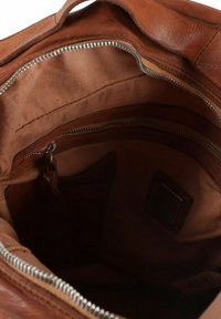 Interno di una borsa in pelle marrone con fodera in tessuto strutturato, tasca con zip e un compartimento aperto per l'organizzazione.