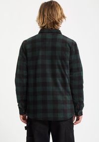 Green and black plaid flannel shirt, long sleeves, classic collar, textured fabric, rounded hem, button cuff detail. Back view.