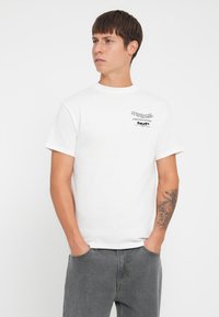 Camiseta de algodón blanca con cuello redondo, mangas cortas y un gráfico impreso en el pecho. El material es suave y tiene un corte casual.
