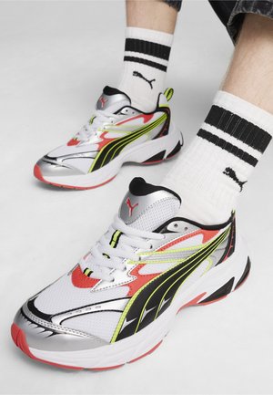 Sneakers Puma z białą siateczką, srebrnymi akcentami, czarno-neonowozielonymi paskami i czerwoną czubką; w połączeniu z czarno-białymi skarpetkami w paski.