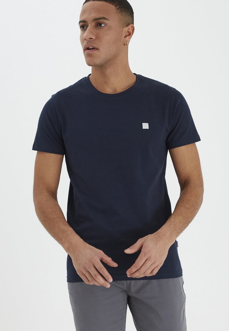 Jūras zils kokvilnas t-krekls ar apaļu kaklu un īsām piedurknēm. Uz kreisā krūškurvja ir neliels kvadrātveida logo. Parasts piegriezums.