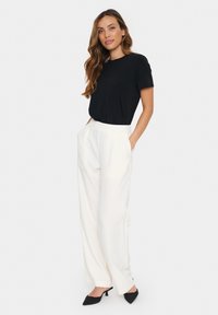 Zwarte t-shirt met korte mouwen, gecombineerd met hoge witte wijde pijpen broek en zwarte puntige hakken, met een gladde textuur en strakke lijnen.