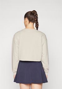 Avskuren beige sweatshirt med långa ärmar, med en rundad halsringning. Matchad med en mörkblå utsvängd kjol som visar en slät tygtextur.