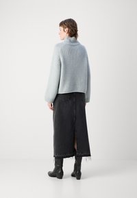 Světle modrý pletený svetr s vysokým límcem, spárovaný s černou denimovou sukní s rozparkem na zadní straně. Černé kotníkové boty dokončují outfit.