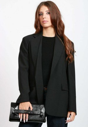 Blazer oversize a righe nere con chiusura a un bottone, abbinato a una pochette nera con texture e un top nero aderente.