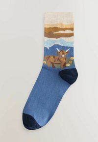 Pletené ponožky s malebným dizajnom krajiny, na ktorom je vyobrazený vysokohorský dobytok, modré pozadie a krémové, hnedé, zelené a tmavomodré akcenty.