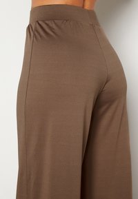 Bruine, aansluitende broek met een hoge, elastische tailleband. De stof is glad en rekbaar, met een subtiele textuur.