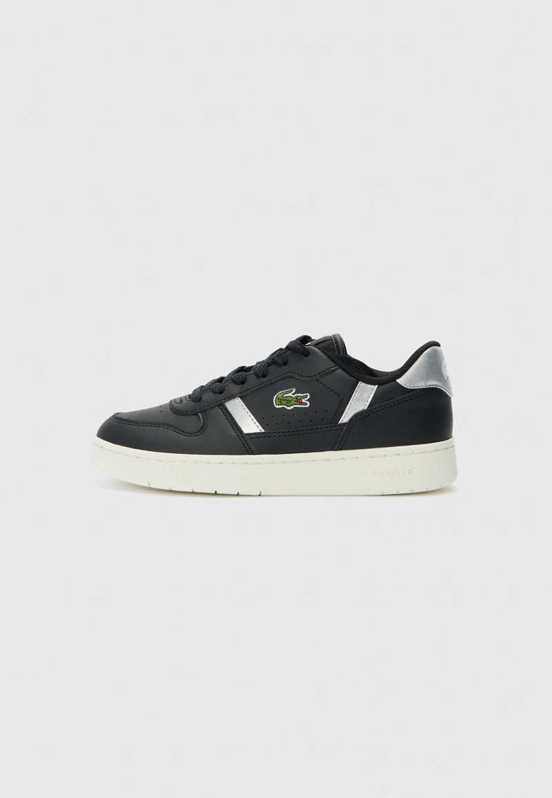 Baskets basses noires avec semelle blanche, accents argentés, lacets noirs et logo crocodile vert sur le côté, présentées sur un fond uni.