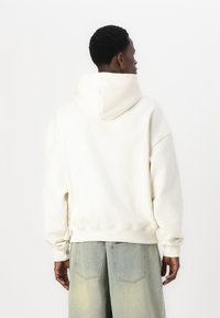Cream-colored hoodie made of soft fabric, featuring a large hood and ribbed cuffs, paired with light denim shorts.