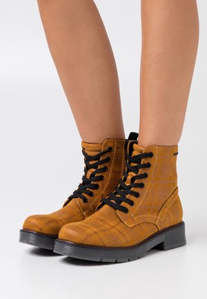 Bruine geruite enkellaarsjes met zwarte veters en een gestructureerde afwerking. Kenmerkend zijn de dikke zwarte zool en de stiksels in contrasterende kleur.
