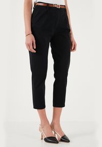 Pantaloni neri a croppati con gamba dritta, realizzati in materiale morbido. Presentano una cintura marrone, indossati con scarpe con tacco bicolori.
