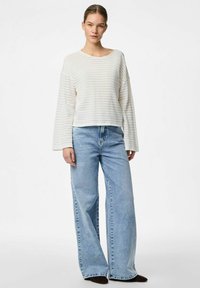 Maglione a righe in cotone color crema con maniche ampie, abbinato a jeans azzurri in denim a vita alta e gamba larga, caratterizzati da un fit rilassato.