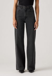 Jean en denim noir taille haute avec une coupe évasée, dotés d'une ceinture tressée et d'un design classique à cinq poches. Texture lisse.