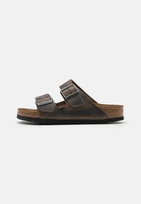 Braune Leder-Sandalen mit zwei verstellbaren Riemen, silbernen Schnallen und einem Korkfußbett. Die Sohle ist schwarz mit einem strukturierten Profil für besseren Halt.