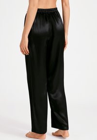 Pantalons de pyjama en satin noir avec une taille élastique, une coupe droite et une texture lisse, présentés de profil et de dos.