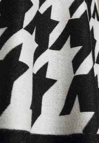 Czarnobiała dzianina z wyraźnym wzorem gwiazd, o teksturowej powierzchni, która zawiera subtelną nitkę brokatową.