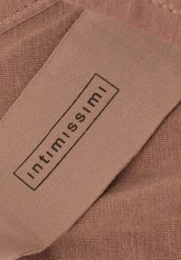 Světlé hnědé látky s hladkým povrchem, s černým obdélníkovým štítkem s nápisem "intimissimi". Viditelné detaily šití.