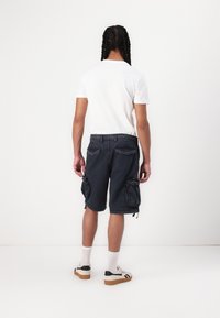 Mørkeblå cargo shorts med flere sidelommer, en afslappet pasform og justerbare snore i kanten, iført en hvid T-shirt og sneakers.