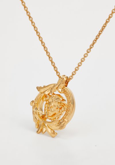 Gold pendant necklace featuring intricate circular design with a face and leaf accents, suspended from a delicate chain.