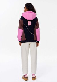 Oversized bluza z kapturem w różowe, brązowe i granatowe panele. Posiada kieszeń typu kangur oraz metkę na plecach z tekstem.