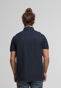 Marineblauwe polo met korte mouwen en een geribbelde kraag. Het materiaal lijkt glad, met een standaard pasvorm. Bevat een klein label aan de zijkant.
