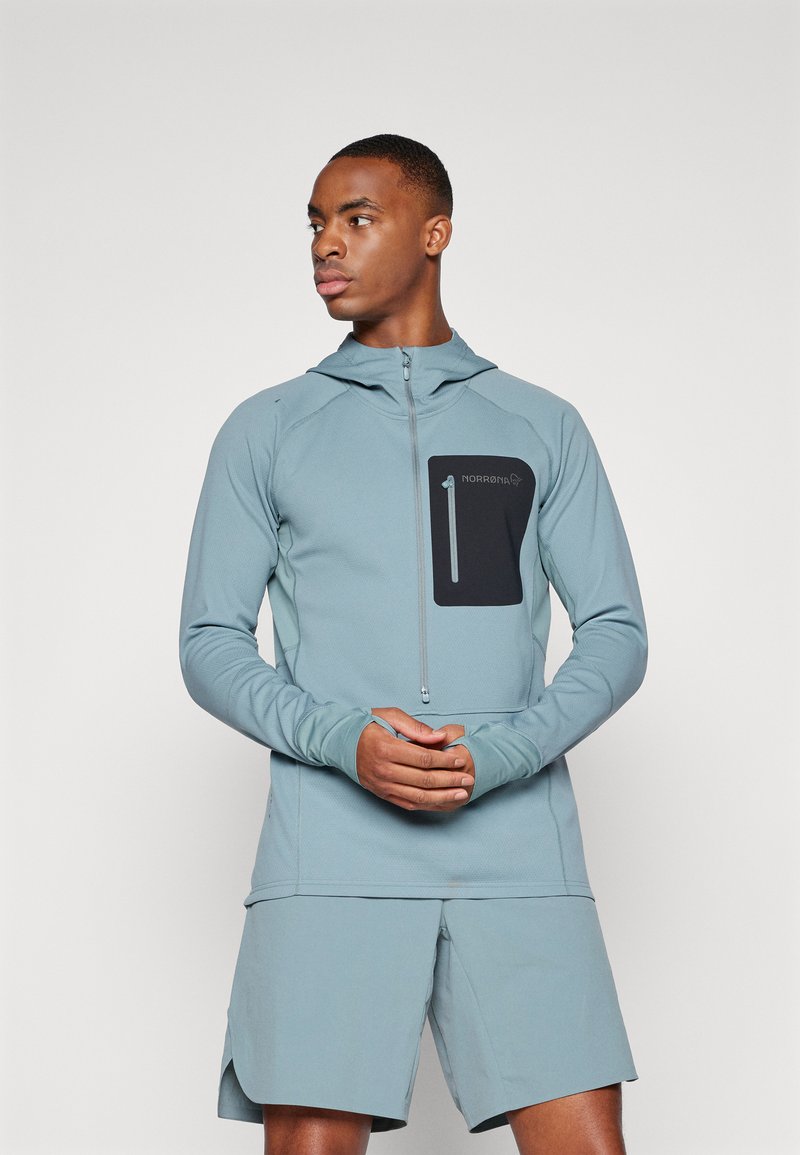 Veste de sport bleu clair avec une fermeture éclair à l'avant, une capuche et une poche poitrine noire. Dispose d'ouvertures pour les pouces aux manches et de shorts assortis.