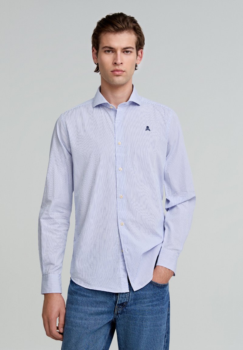 Himmelblau gestreiftes Hemd mit Button-Down-Kragen, langen Ärmeln und kleinem marineblauen Logo auf der Brust. Kombination mit blauen Jeans.