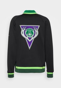 Chaqueta negra con cuello y puños en verde y verde claro, con un logo en forma de triángulo púrpura que presenta un balón de baloncesto verde y cuernos blancos en la parte posterior.