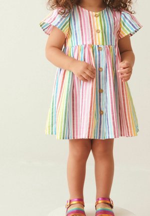 Gestreiftes Kleid mit kurzen, flatternden Ärmeln, in sanften Farben und Holzknöpfen auf der Vorderseite. Getragen mit mehrfarbigen Sandalen.