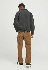 Chaqueta de mezclilla negra con un cuello acanalado, combinada con pantalones cargo de pana marrones con bolsillos. Zapatillas negras y blancas completan el look.