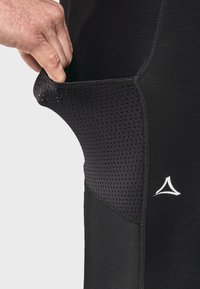 Schwarze sportliche Leggings mit einer Netzseitentasche, glatter Textur, weißem Logodetail und verstärkten Nähten.