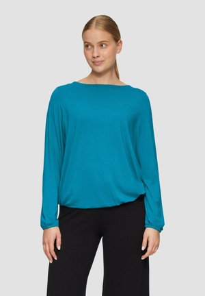 Teal langwerpige top met een bootnek, relaxte pasvorm en gathered manchetten. Het materiaal lijkt zacht met een gladde textuur. Zwarte broek wordt eronder gedragen.
