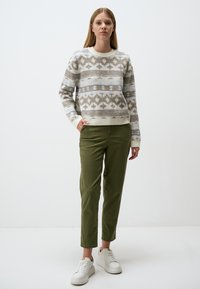 Sweater in light cream with geometric grey and beige patterns, paired with green tapered pants and white sneakers, creating a casual look.