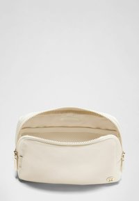 Bolsa cremosa con cremallera hecha de tela suave, con herrajes dorados y un bolsillo de malla en el interior para organizar.