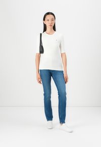 White ribbed short-sleeve top paired with blue denim jeans. White sneakers and a small black shoulder bag complete the outfit.