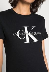 Svart bomullströja med en stor vit "CK"-logotyp och texten "CALVIN KLEIN JEANS" i en elegant, modern stil framtill.