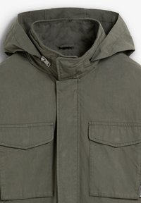 Chaqueta verde oliva con capucha, que presenta una cremallera frontal, dos bolsillos en el pecho y una textura suave y mate.
