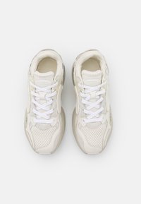 Paire de baskets blanches avec des panneaux en mesh et en cuir, des lacets blancs et des semelles rembourrées, vues de dessus sur un fond uni.